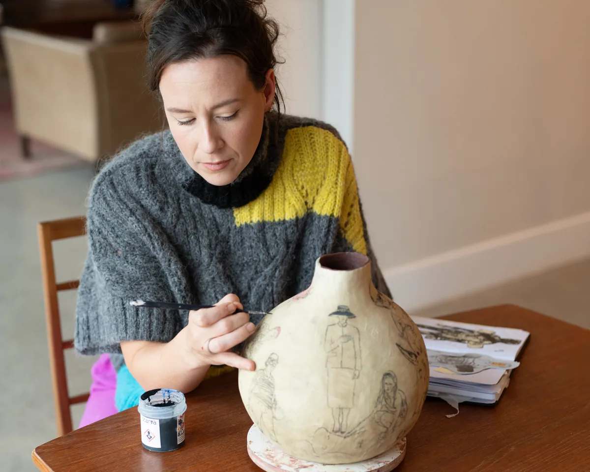 Suzanne Dolan drawing on a hand-built vessel at her table