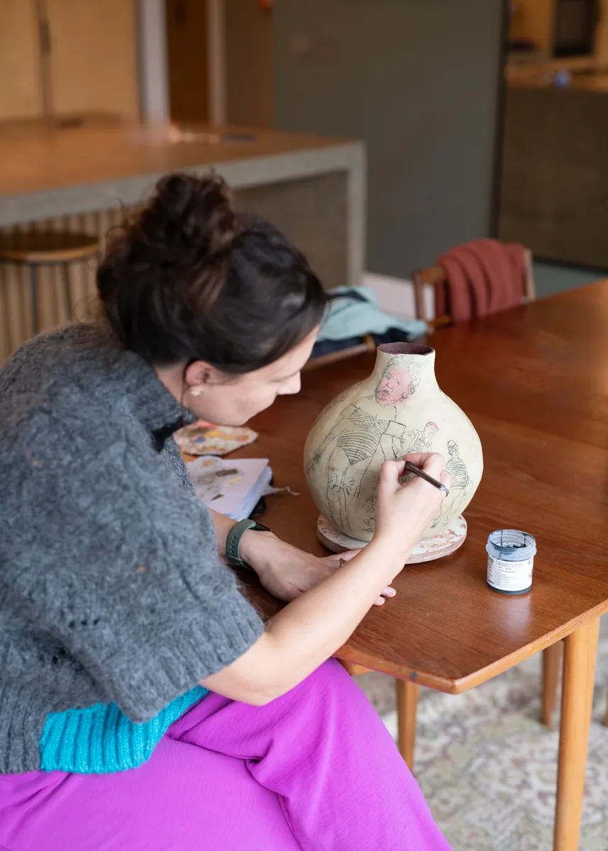 Suzanne Dolan at her table with a vessel and brushes